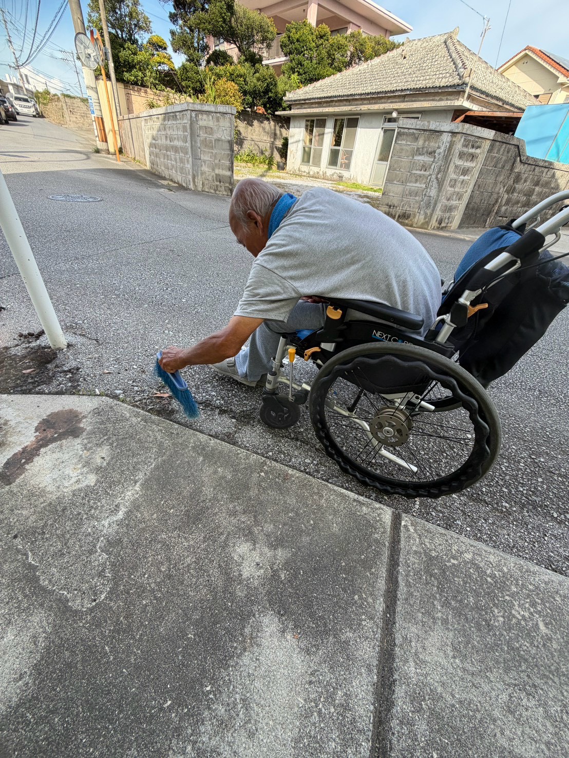 車椅子の利用者が屋外で歩道を掃除している様子